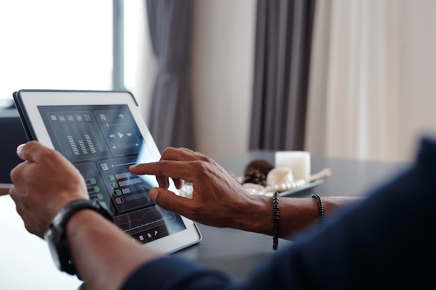 Photo hands of man using smart home application on tablet computer to control music volume in apartment