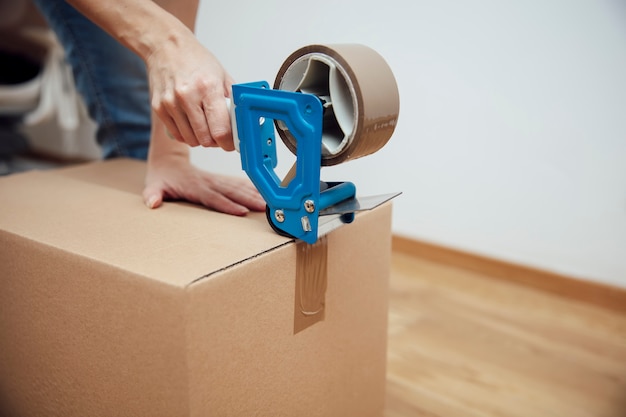 Hands of a man using a tape dispenser to seal a shipping box