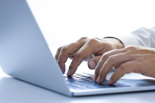 Hands of a man with white shirt typing on a laptop or notebook computer on a desktop while working in the office using internet