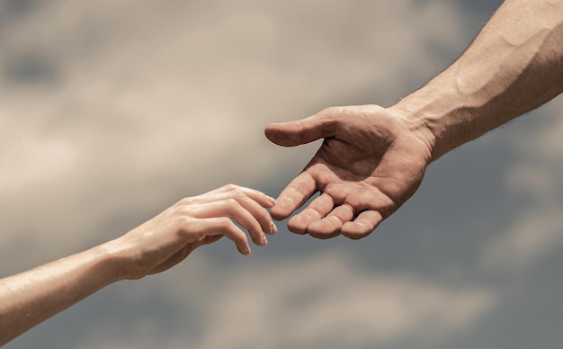 Hands of man and woman on blue sky background. Lending a helping hand. Giving a helping hand. Solidarity, compassion, and charity, rescue. Hands of man and woman reaching to each other, support.