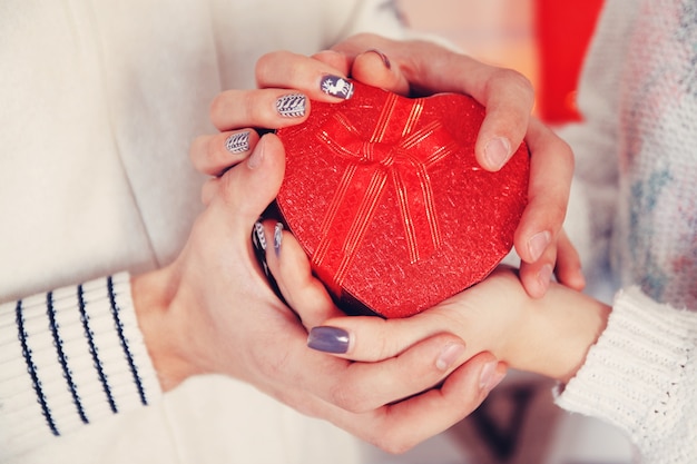 Hands of a man and woman holding a heart-shaped box