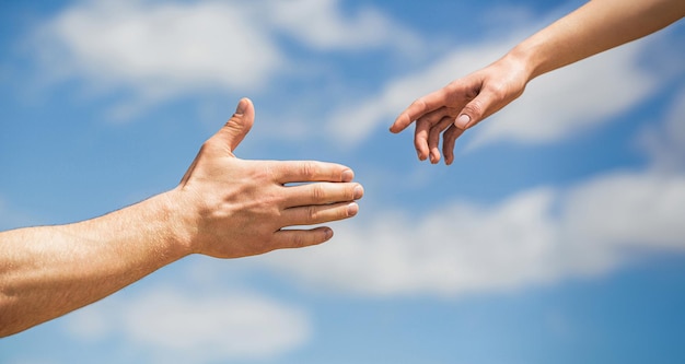 Hands man and woman reaching to each other support Giving a helping hand Hands of man and woman on blue sky background Lending a helping hand