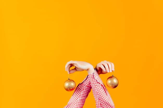 Hands of a man on a yellow background, which are holding new year's toys, balls of golden color