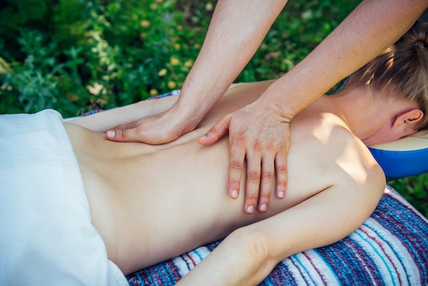 Hands masseur on the back of an unrecognizable patient close-up. Relaxed woman receives wellness massage at the Spa center outdoor