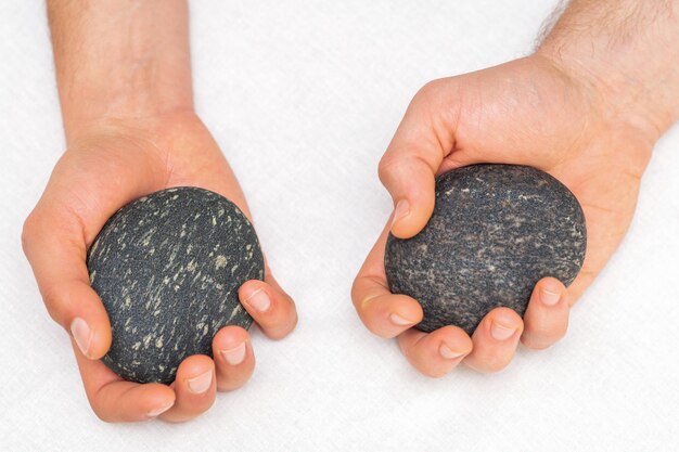 Hands of masseur holding massage stones on white background, top view.