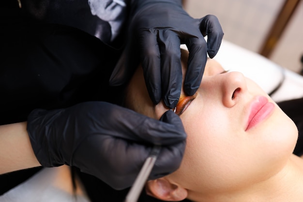 The hands of the master close - up apply a special roller for curling cilia to the client's eyelid