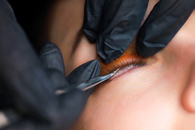 The hands of the master close up correct the eyelash glued to the roller with special tweezers