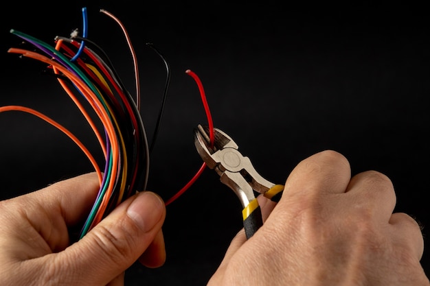 Hands of the master hold wire cutters and wire closeup on black background. Electronics Repair Idea