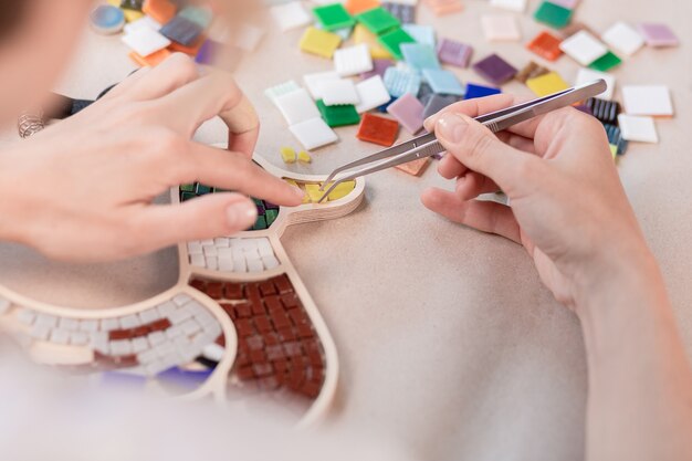 Hands of master working on new modern colorful mosaic. Close-up