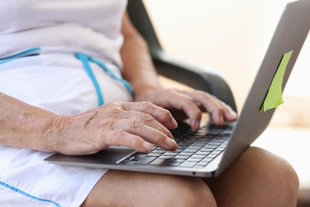 Hands of mature elderly woman are typing on laptop searching for information on internet and