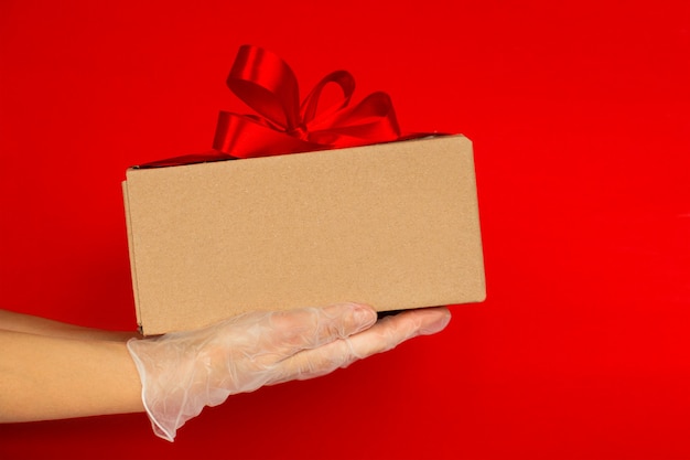 Photo hands in medical gloves holding a gift box with a red ribbon