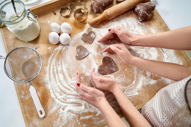 Hands of mom and daughter making heart shape on pastry board