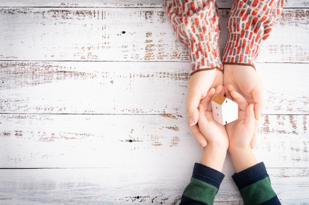 Photo hands of mother and child gently hold a beautiful white wooden toy house with care show the feeling of family love and protecting. home loan, insurance, property investment, security. copy space.