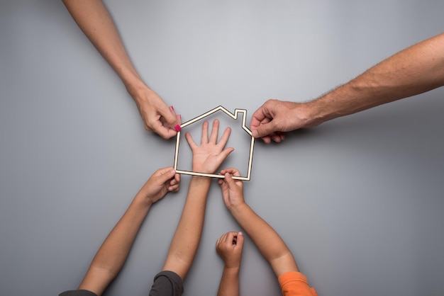 Hands of a mother father and two kids holding the framework of a house