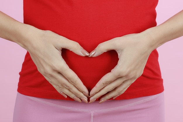 Hands of a mother putting on belly in heart sign or symbol Concept of love care and woman awaiting for coming newborn baby Closeup shot