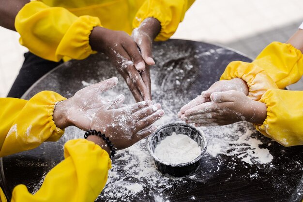 Hands of multinational children cooks play with flour for dough and having fun closeup young cooks children cooking khachapuri
