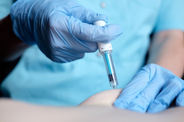 Hands of nurse in blue surgical gloves making injection of anticoagulant subcutaneously