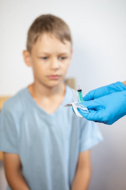 the hands of a nurse in gloves open a pack of syringes closeup in front of a boys face