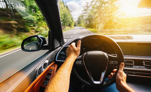 写真 ハンドルの車の運転手の手、田舎道で夏の日に車を運転し、ツアーの旅で空の高速道路を運転するのを楽しんでいます-pov、一人称ビューショット