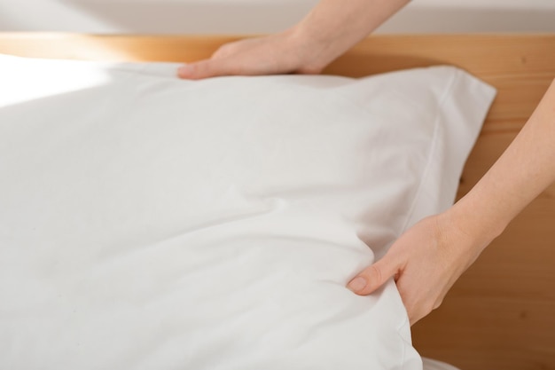 写真 白人のミレニアル世代の女性の手が快適なベッドに柔らかい白い枕を置き、ベッドを作る