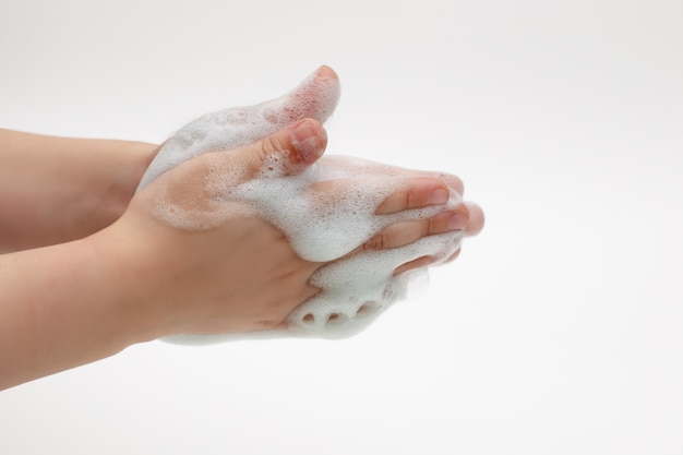 Руки ребенка на белом фоне в белой пене из антибактериального мыла