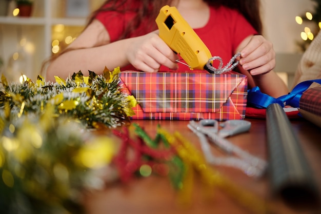 사진 뜨거운 아교 총으로 포장 된 선물에 반짝이 활을 붙이는 소녀의 손