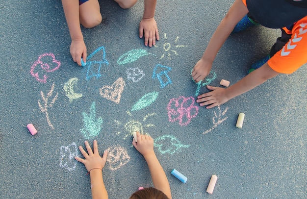 写真 女の子と男の子の手が歩道でチョークで絵を描いている