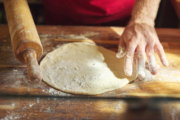 木製のテーブルの上に食べ物を準備する小麦粉の生地と男性のパン屋の手