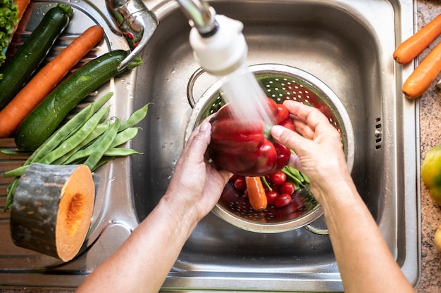 Фото Руки женщины, моющей свежий урожай овощей на кухне, тонут под струей воды