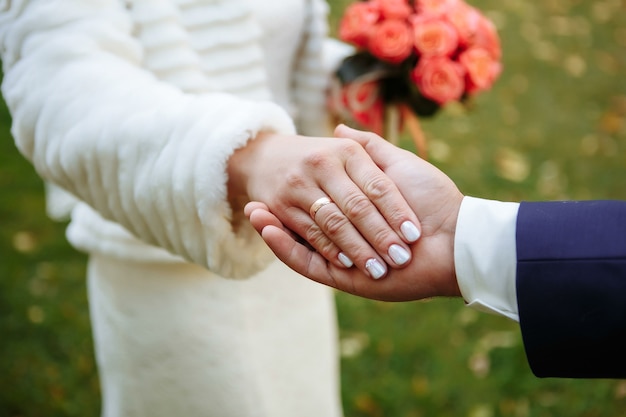 Mani o mani di sposi con fedi nuziali e bouquet da sposa