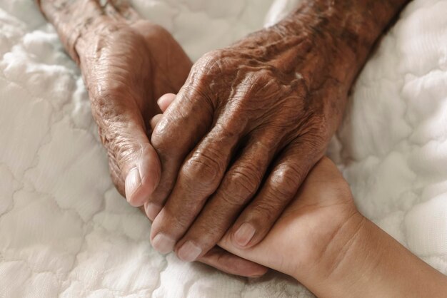 Photo hands of the old man and a child's hand on the white bed