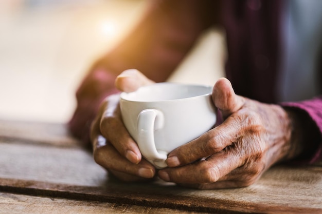 Руки старика, держащего чашку кофе на деревянном столе, винтажный тон
