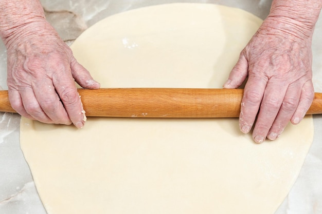 Hands of the old woman roll the dough on a marble table