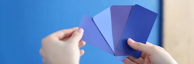 Photo in hands of palette with blue shades against blue wall selection of paint for walls and facades