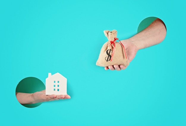 Hands in the paper holes holding house and a bag with money