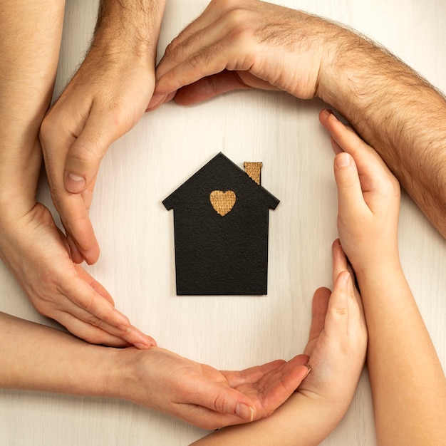 Hands of parents and child surround the layout of a dark house on a light background