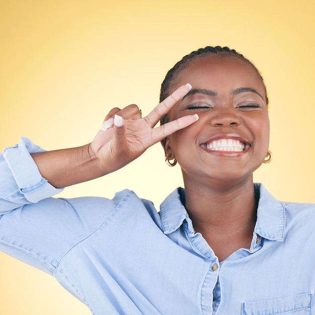 hands peace sign and face of black woman in studio smile for confidence glow and beauty excited hand gesture and african person on yellow background with cosmetics makeup and glamour and emoji
