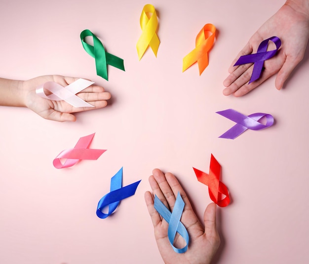 Hands of people holding colorful ribbons on pink background cancer awareness World cancer day National cancer survivor day world autism supported living and illness Prostate awareness concept