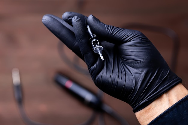 The hands of a permanent makeup artist in black medical gloves on which lies a disposable cartridge for a tattoo machine