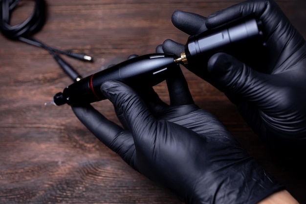 The hands of the permanent makeup artist in black sterile gloves he tries to connect the wireless battery pack of the tattoo machine