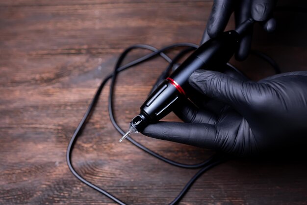 The hands of a permanent makeup artist in black sterile gloves hold a tattoo machine with a cartridge on it