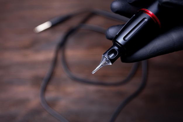 The hands of a permanent makeup artist in black sterile gloves shows a closeup of a tattoo machine on which a tattoo cartridge is worn