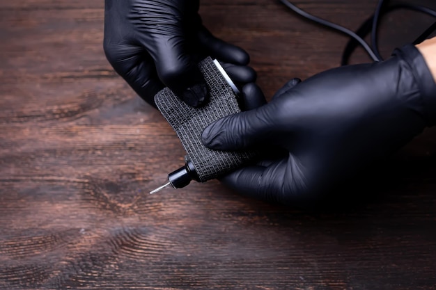 The hands of a permanent makeup artist in black sterile gloves stretch a black bandage tape to protect the tattoo machine wrapped around her