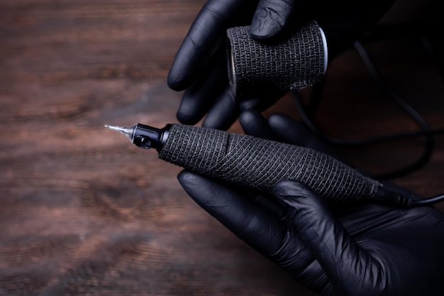 黒の滅菌手袋をしたアートメイクマスターの手は、タトゥーマシンを包帯テープと黒の色で包み、それを引き裂こうとします