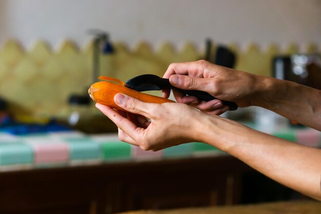 Hands of a person peeling a carrot in the kitchen.