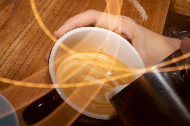 Hands of a person pouring milk into a coffee cup with lines of light paint