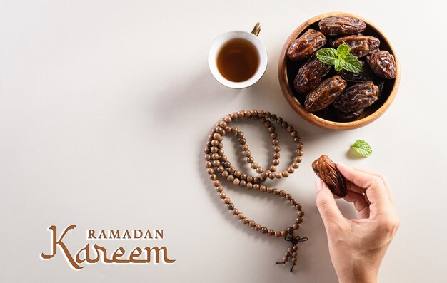 Photo hands picking up dates fruit tea and rosary beads with ramadan kareem text