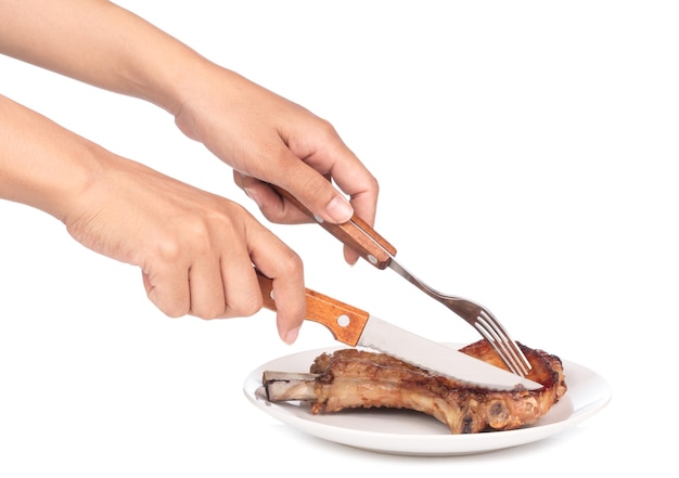 Hands picking up a grilled pork rib by fork and knife isolated\
on white background