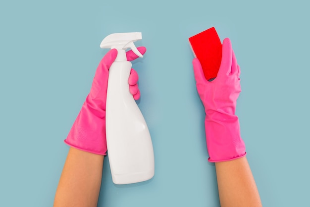 Руки в розовых перчатках держат дозатор моющего средства и мочалку. Синий фон. Концепция очистки.