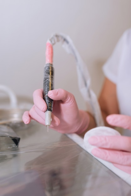 Руки в розовых латексных медицинских перчатках с инструментами для перманентного макияжа